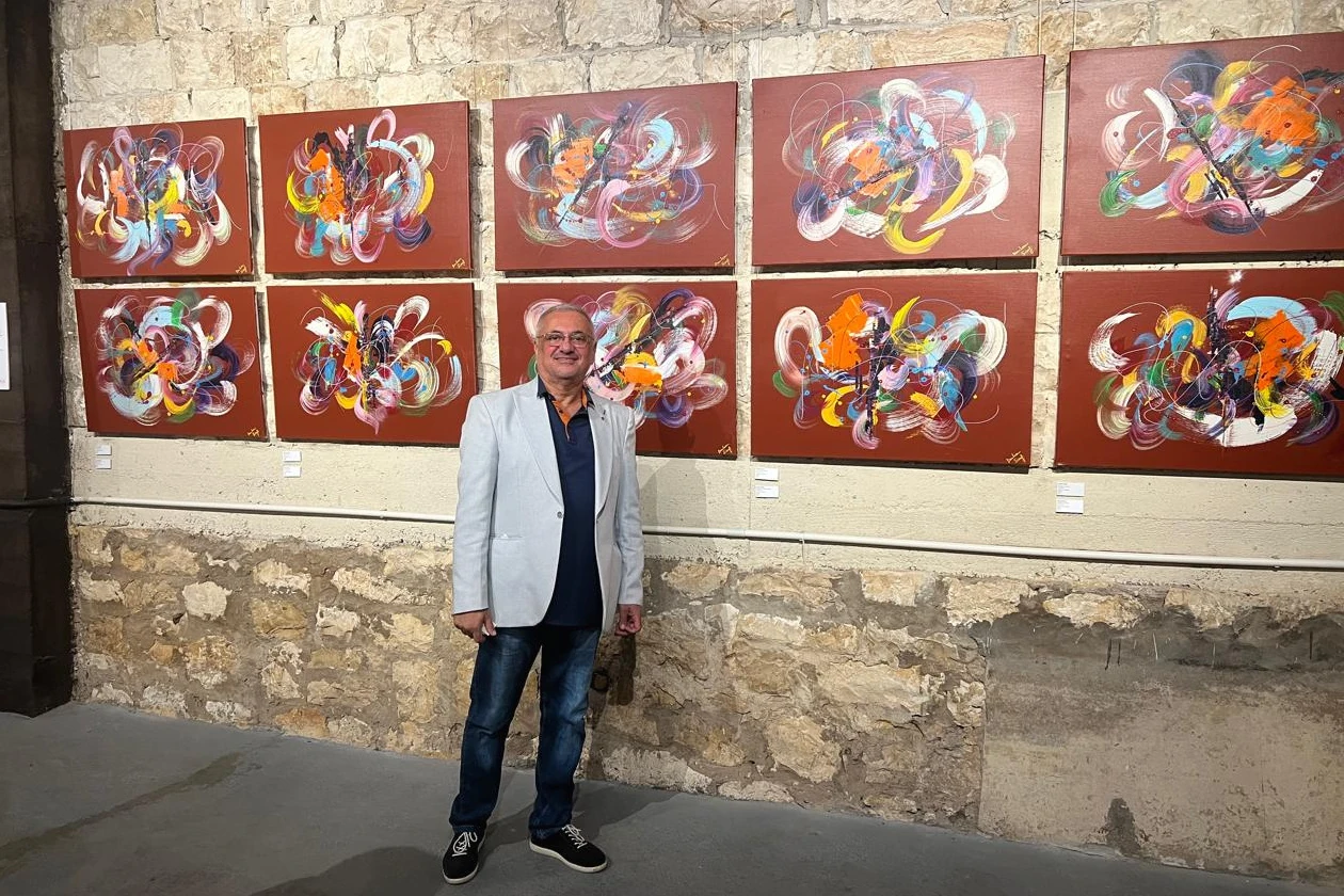 Don Léon Sioufi frente a su serie de lienzos abstractos sobre fondo rojo